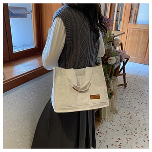 Detail of white corduroy tote bag featuring leather label and external front pocket