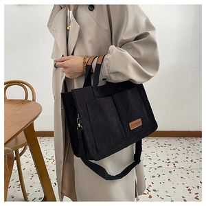Black corduroy tote bag detail showing dual front pockets and brown fashion leather label