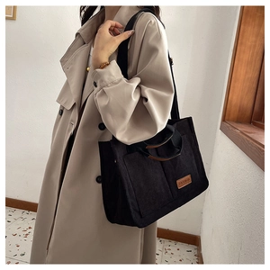 Detail of black corduroy tote bag with leather fashion tag and wide shoulder strap