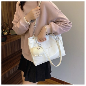 Detail of white leather tote bag with chain strap and plush charm worn by a model