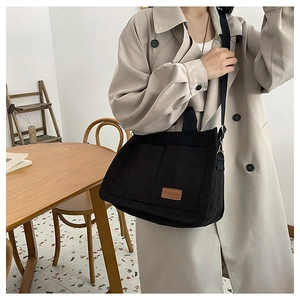 Close-up of black corduroy tote bag with large front pockets and brown fashion patch