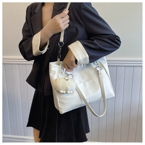 Detail of white leather tote bag featuring a cute plush charm and silver chain strap