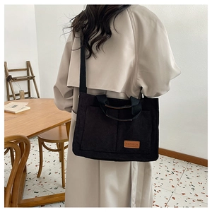 Detail of black corduroy tote bag with leather label worn by model in minimalist setting