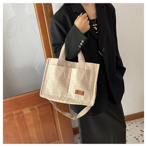Detail of beige corduroy tote bag showing front pockets and brown fashion leather label