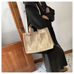 Model showcasing a beige corduroy tote bag with dual handles and long shoulder strap