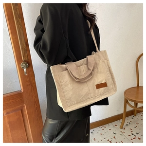 Model wearing a large beige corduroy tote bag with wide strap in a modern home setting
