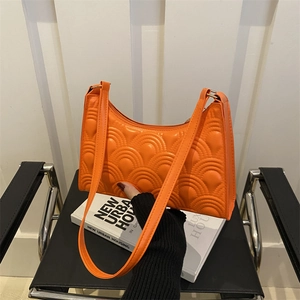 Bright orange baguette bag with scalloped quilting on a modern chair