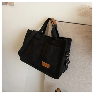 Detail of black corduroy tote bag showing front pockets and brown leather brand patch