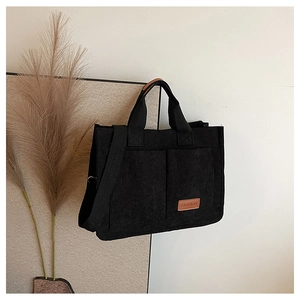 Detailed shot of black corduroy tote bag showing front pockets and fashion leather label