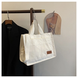 White corduroy tote bag detail with fashion leather patch hanging on a wooden rack