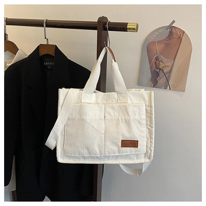 Detail of white corduroy tote bag featuring front pockets and brown FASHION leather patch