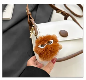 Detail of a white leather crossbody bag featuring a fluffy brown monster charm accessory