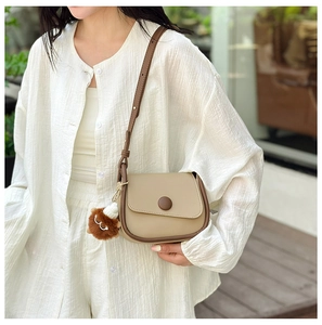 Detail of a beige and brown contrast crossbody bag with a cute lion plush charm