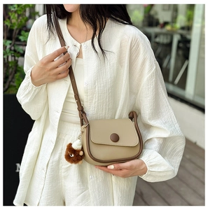 Detail of vintage saddle bag in khaki leather with brown trim and plush bear charm