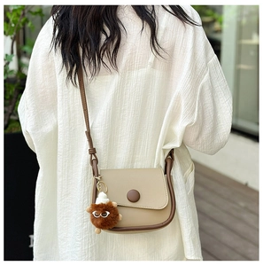 Detail of a khaki saddle bag with brown trim and a plush monster charm on a strap