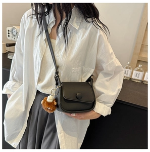 Close-up of black leather saddle bag with round buckle and brown fur charm on model
