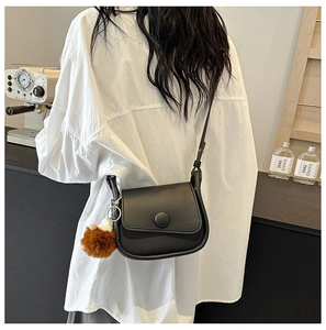 Detail of minimalist black leather saddle bag with plush pom-pom and shoulder strap