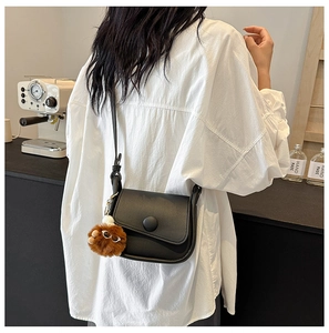 Detail of black leather crossbody bag with round buckle and brown plush charm accessory