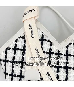 Detail of black and white tweed tote bag showing cotton strap with letter branding