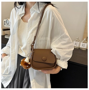 Detail view of a vintage brown crossbody bag with flap cover and plush ball charm on a model