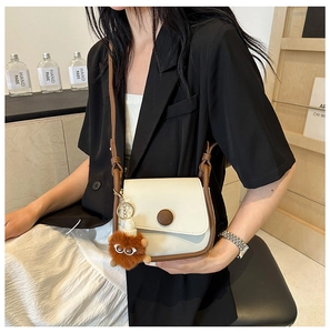 Detail of a color-block crossbody bag with a round buckle and a cute plush monster charm