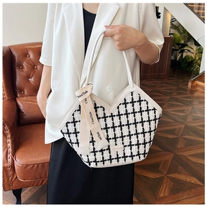 Detail of tweed check tote bag with white leather handles and ribbon on sofa