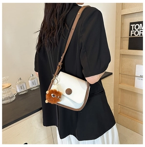 Detail of contrast color crossbody bag with ivory and caramel panels and plush charm