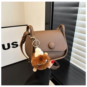 Close-up of a brown saddle bag featuring smooth faux leather and a cute plush charm