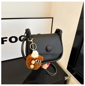 Detail view of black matte leather crossbody bag with a plush brown doll pendant