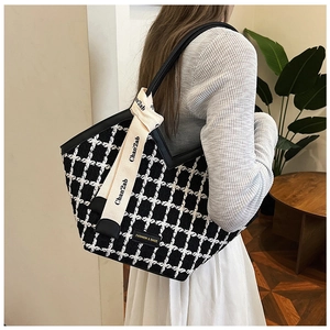 Detail of black and white tweed tote bag featuring leather trim and decorative ribbon strap