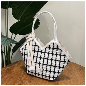 Detail of checkered tweed tote bag with leather trim and decorative silk ribbon on a table