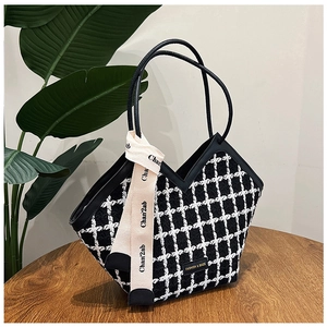 Detail of black and white tweed tote bag with elegant silk scarf and slim handles on wood