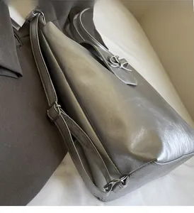 Detail of silver faux leather shoulder bag featuring a decorative bow and adjustable strap