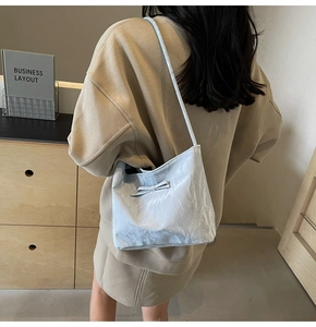 Dettaglio della borsa a spalla azzurra con trama stropicciata e fiocco su una modella