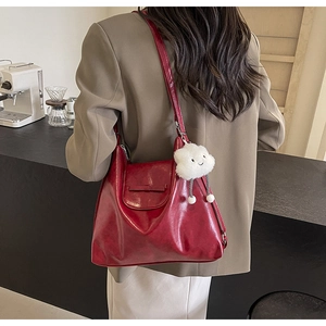 Deep red glossy tote bag with adjustable strap and plush cloud pendant on a model