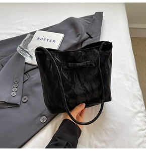 Détail d'un sac cabas noir plissé avec nœud sur un décor de lit au style minimaliste