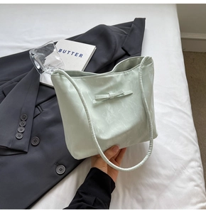Détail d'un sac cabas texturé vert menthe avec nœud assorti sur une literie blanche