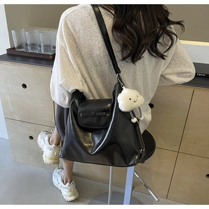Detail of a large black soft leather shoulder bag with a cute white plush cloud charm