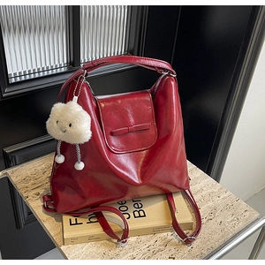 Close-up of deep red patent leather bag with a bow decoration and plush cloud charm