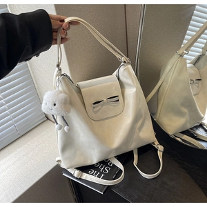 Detail of cream white faux leather tote bag with black bow and plush cloud pendant