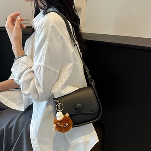 Retro black leather shoulder bag with plush charm and flap closure shown on model