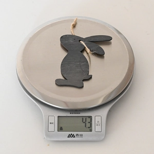 Detail of lightweight black wooden rabbit pendant with jute rope on a digital scale