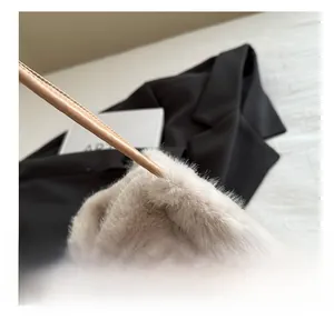 Detail shot of plush beige faux fur tote bag with brown leather strap on black coat