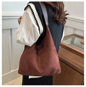 Close-up of a large brown suede tote bag worn over the shoulder by a model indoors