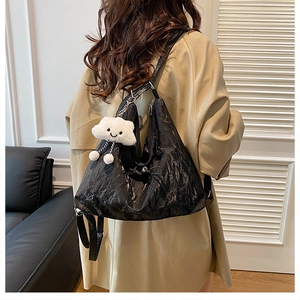 Detail of black pleated tote bag with cloud plush pendant worn on casual khaki coat