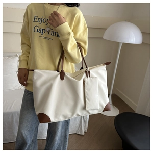 Close-up of a large beige tote bag with brown leather handles and a matching mini pouch
