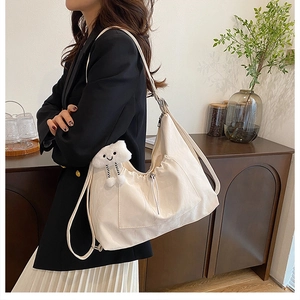 Detail showing creamy white large tote bag with cloud charm on model in a cafe setting