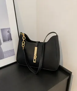 Detail einer schwarzen Halbmond-Tasche mit goldenem Verschluss und Kettenelementen