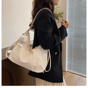 Model wearing a large cream tote bag with drawstring closure and cute cloud pendant