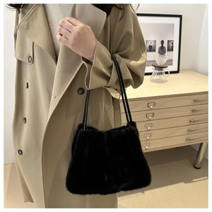 Detail of a plush black faux fur shoulder bag with leather straps on a beige coat